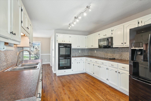 kitchen featuring black appliances, white cabinets, wood finished floors, and a sink