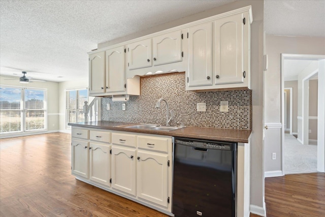 kitchen with dark countertops, black dishwasher, decorative backsplash, wood finished floors, and a sink