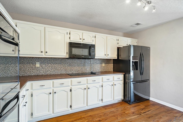 kitchen with dark countertops, visible vents, light wood finished floors, black appliances, and white cabinetry