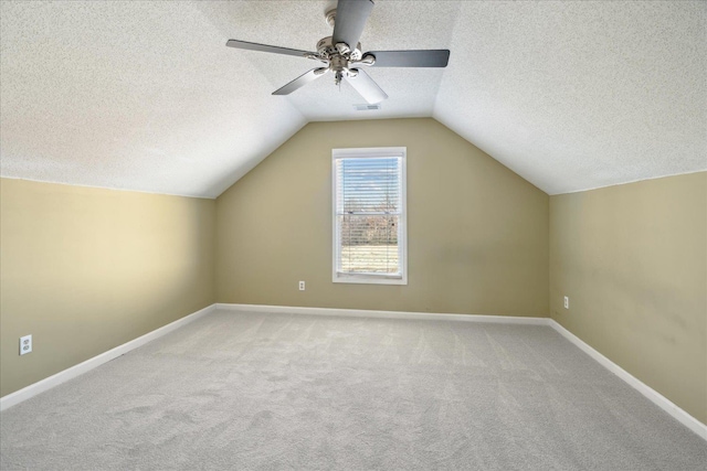 additional living space with visible vents, carpet, baseboards, vaulted ceiling, and a textured ceiling