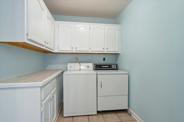 laundry room featuring a textured ceiling, cabinet space, light tile patterned floors, baseboards, and washing machine and clothes dryer