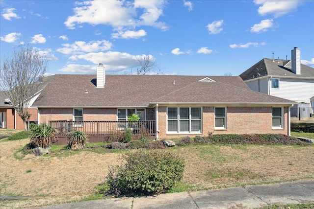 back of property featuring brick siding, a wooden deck, a chimney, and a shingled roof