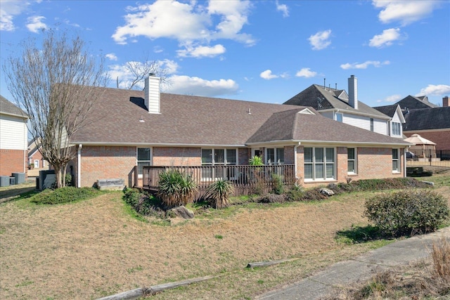 rear view of property with brick siding, a shingled roof, cooling unit, a chimney, and a deck