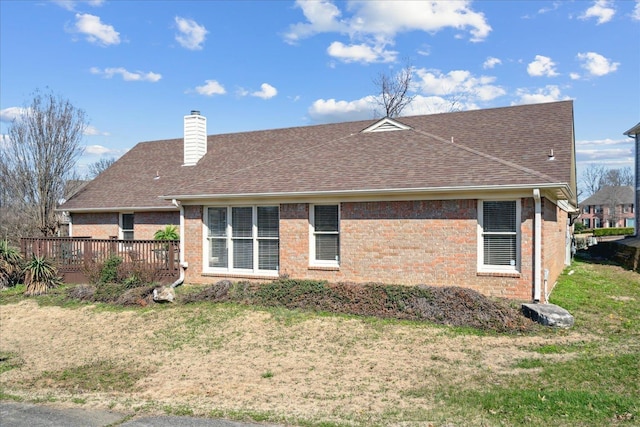 rear view of property with brick siding, a lawn, and a chimney