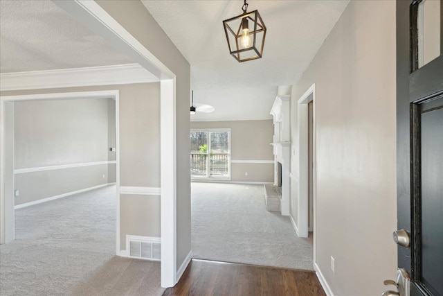 corridor featuring visible vents, baseboards, carpet, and a textured ceiling