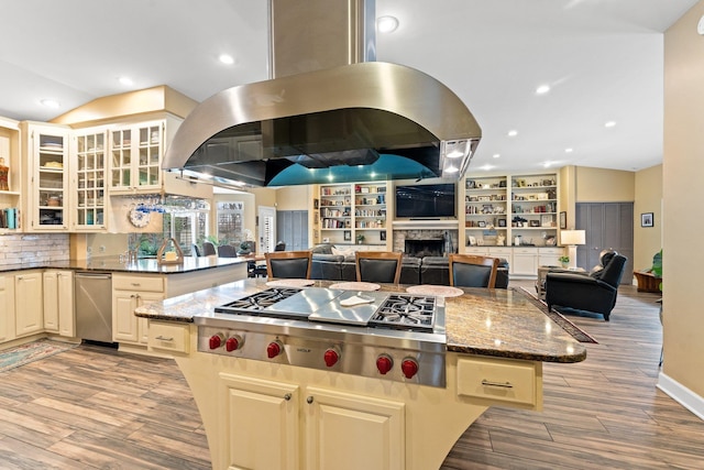 kitchen featuring a kitchen island, stainless steel gas cooktop, a fireplace, cream cabinets, and island exhaust hood