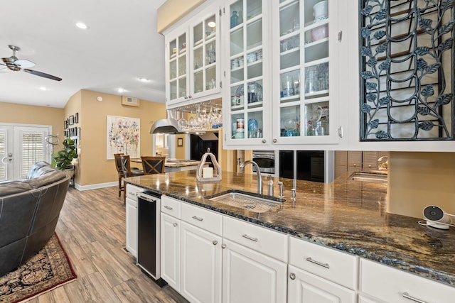 kitchen with glass insert cabinets, open floor plan, light wood-type flooring, a ceiling fan, and a sink