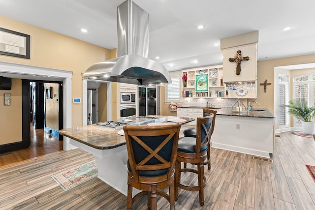 kitchen with tasteful backsplash, appliances with stainless steel finishes, island range hood, white cabinets, and open shelves