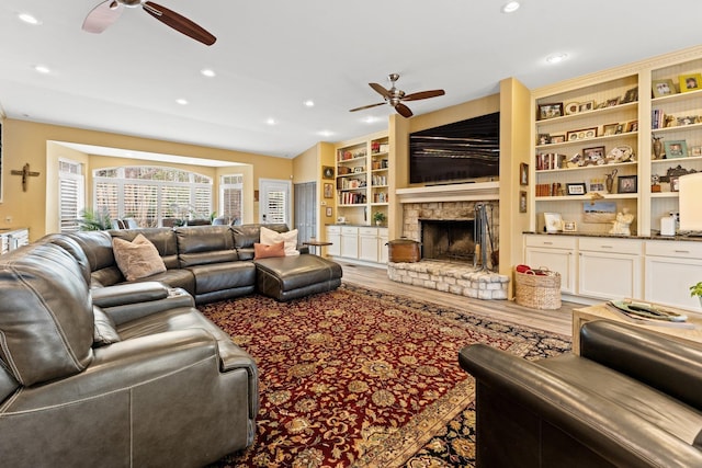 living room featuring a fireplace with raised hearth, a ceiling fan, built in features, wood finished floors, and recessed lighting