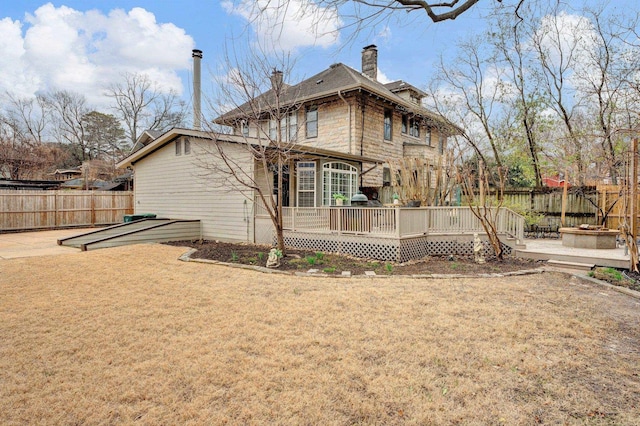 back of property with an outdoor fire pit, a yard, a fenced backyard, a chimney, and a deck