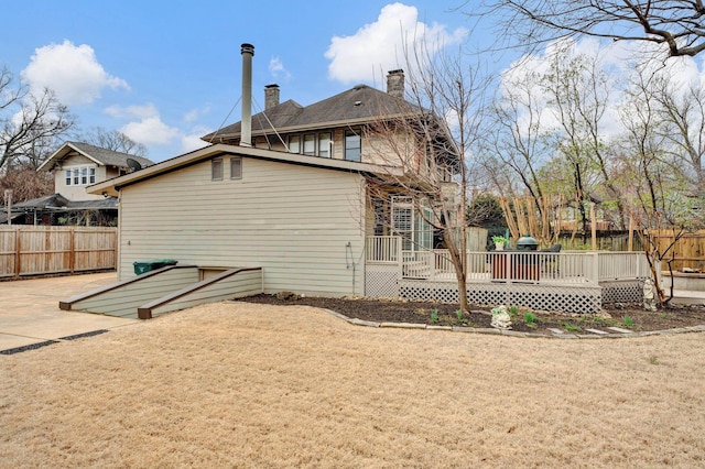 back of property featuring a yard, a deck, a chimney, and fence