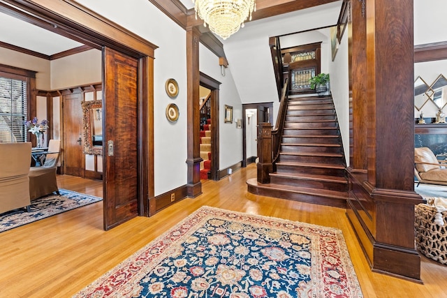 foyer entrance featuring baseboards, stairs, crown molding, a notable chandelier, and light wood-type flooring