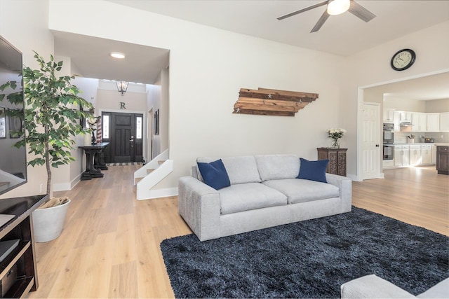 living room featuring stairway, baseboards, light wood-style floors, and a ceiling fan