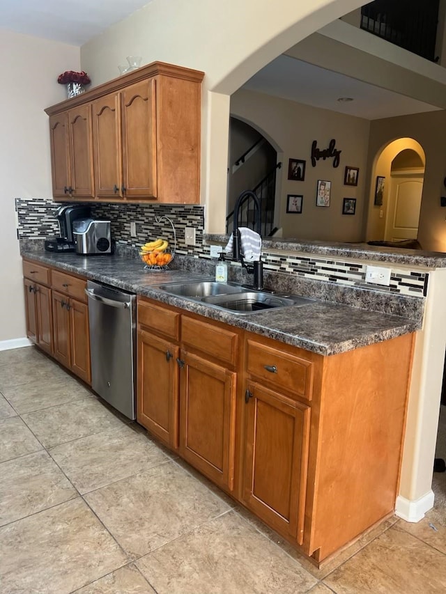 kitchen with backsplash, a peninsula, stainless steel dishwasher, brown cabinetry, and a sink