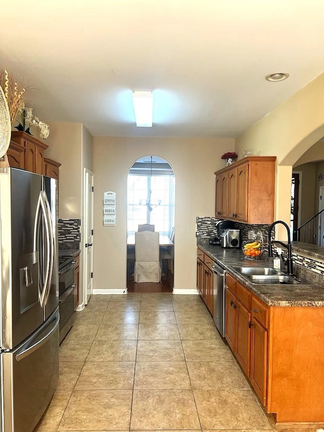 kitchen with tasteful backsplash, baseboards, arched walkways, stainless steel appliances, and a sink