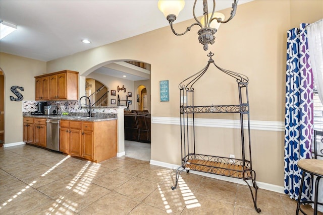 kitchen with brown cabinetry, dishwasher, stone counters, arched walkways, and a sink