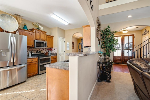 kitchen featuring backsplash, brown cabinetry, arched walkways, and appliances with stainless steel finishes