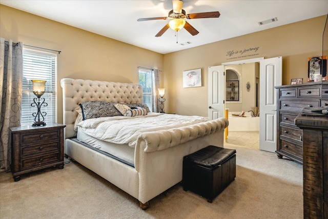 bedroom with visible vents, light colored carpet, ensuite bathroom, and a ceiling fan