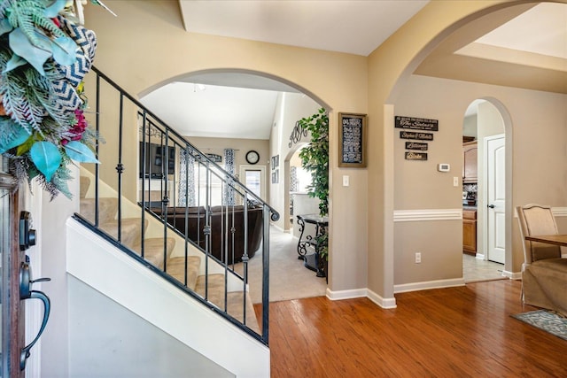 foyer with baseboards, arched walkways, wood finished floors, and stairs