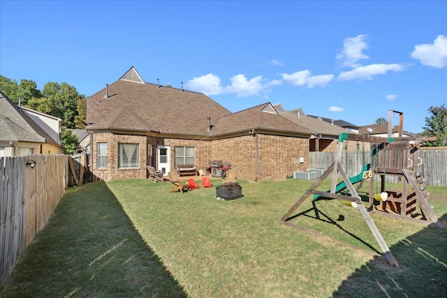 rear view of property with brick siding, a fire pit, a playground, and a fenced backyard