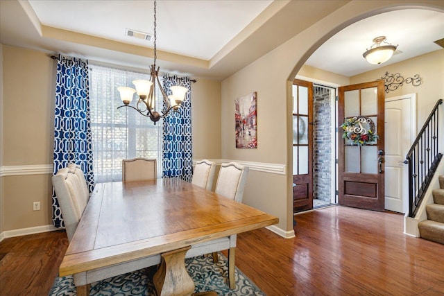 dining area featuring arched walkways, visible vents, stairway, and wood finished floors