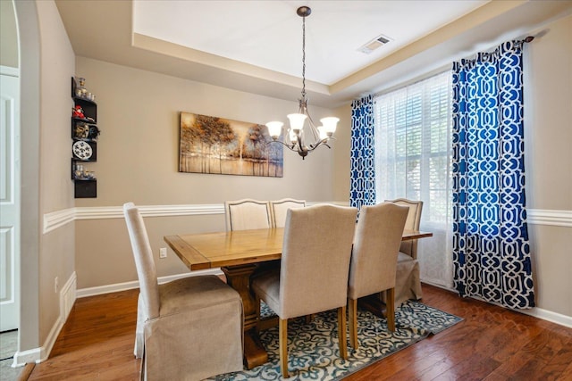 dining room with visible vents, a raised ceiling, an inviting chandelier, and hardwood / wood-style floors