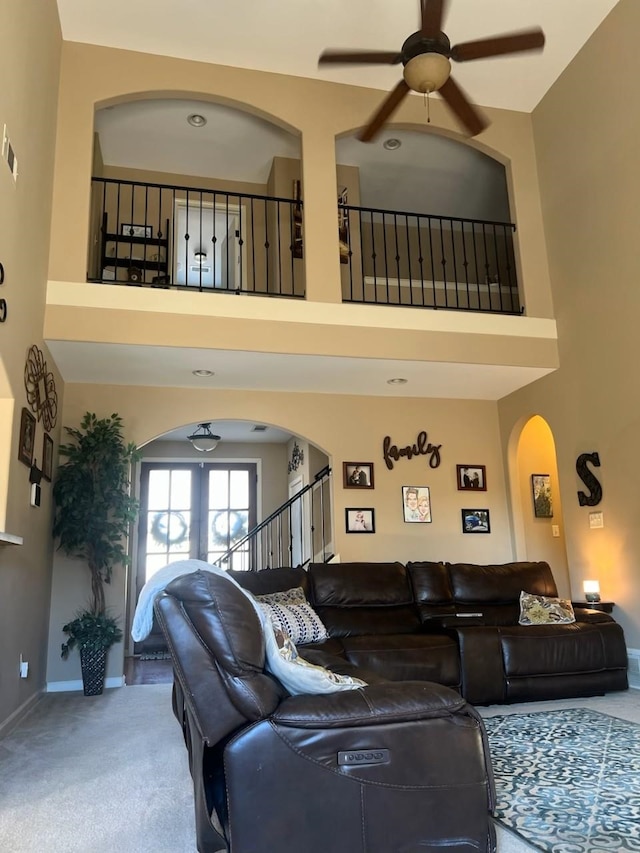 carpeted living room with visible vents, a high ceiling, arched walkways, ceiling fan, and stairs