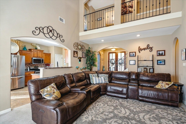 living room featuring light carpet, visible vents, arched walkways, and a high ceiling