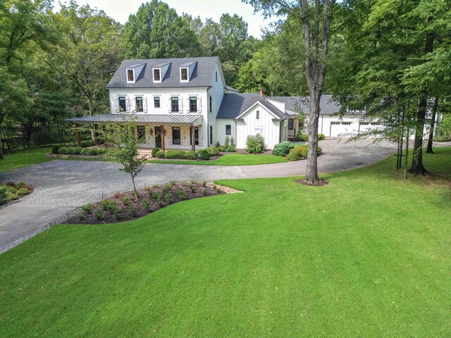 view of front of property featuring a porch, driveway, a standing seam roof, and a front lawn