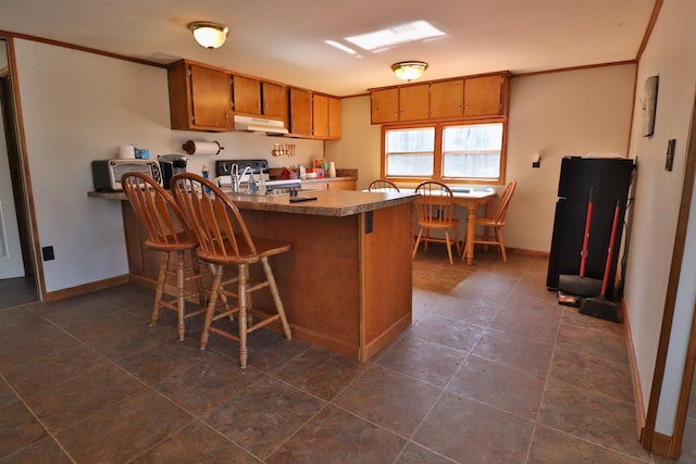 kitchen with under cabinet range hood, brown cabinets, a peninsula, and ornamental molding