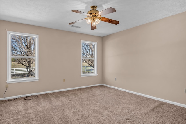 carpeted spare room featuring visible vents, a ceiling fan, and baseboards