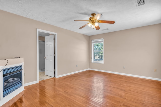 unfurnished living room featuring light wood-type flooring, visible vents, a textured ceiling, and a fireplace