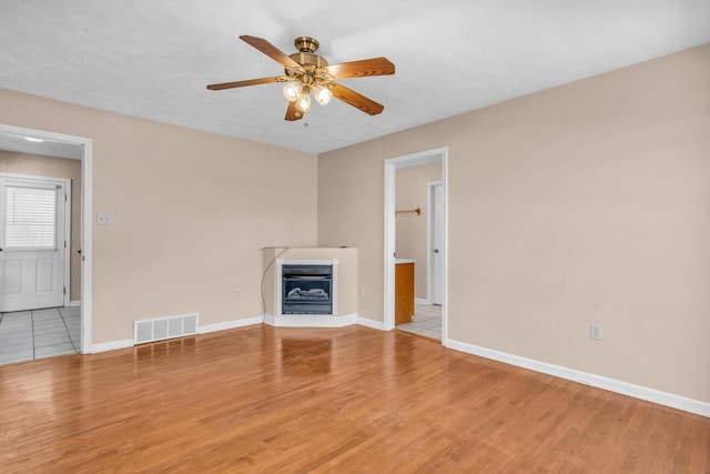 unfurnished living room with visible vents, baseboards, light wood-type flooring, a glass covered fireplace, and a ceiling fan