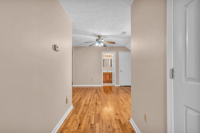 corridor featuring visible vents, baseboards, a textured ceiling, and light wood finished floors