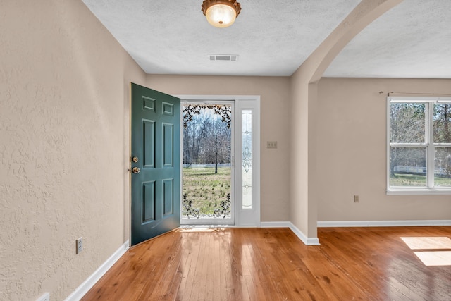 foyer entrance featuring arched walkways, visible vents, a textured wall, and hardwood / wood-style flooring