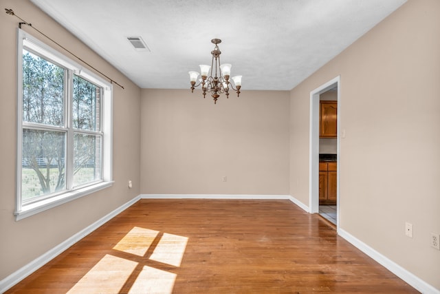 empty room featuring a notable chandelier, baseboards, visible vents, and light wood finished floors