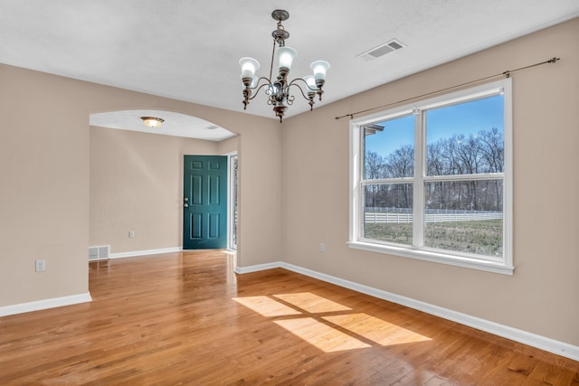 empty room with baseboards, arched walkways, visible vents, and light wood-type flooring