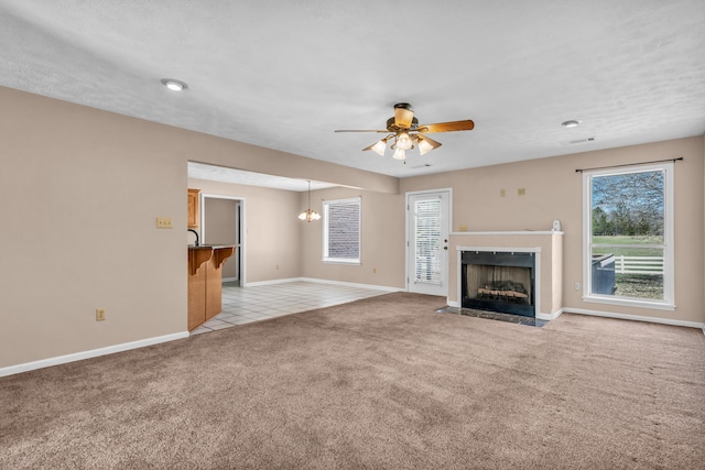 unfurnished living room featuring light tile patterned floors, baseboards, a fireplace with flush hearth, light carpet, and ceiling fan with notable chandelier