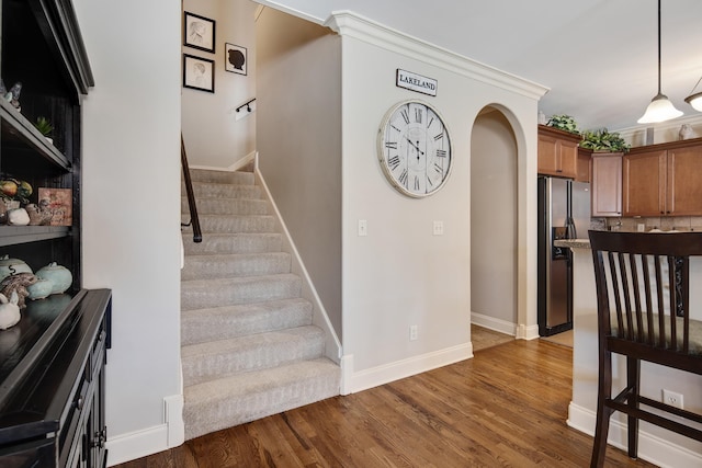 staircase with arched walkways, baseboards, and wood finished floors