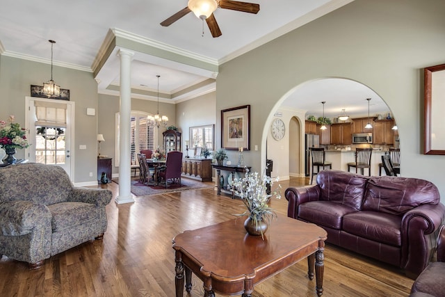 living room featuring wood finished floors, baseboards, ornate columns, crown molding, and ceiling fan with notable chandelier