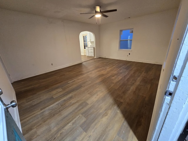 interior space featuring dark wood-type flooring, a ceiling fan, arched walkways, and baseboards