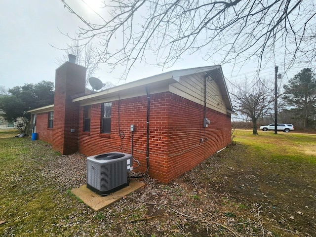 view of side of property with brick siding, central AC unit, and a chimney