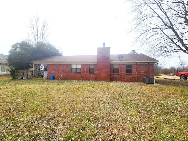 rear view of property featuring cooling unit, brick siding, a chimney, and a lawn