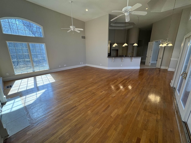 unfurnished living room featuring visible vents, baseboards, ceiling fan with notable chandelier, a towering ceiling, and wood finished floors