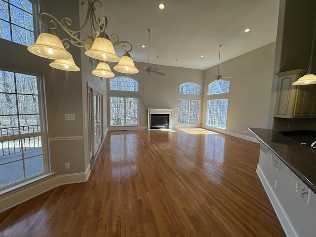 unfurnished living room with ceiling fan, baseboards, a fireplace, a towering ceiling, and wood finished floors