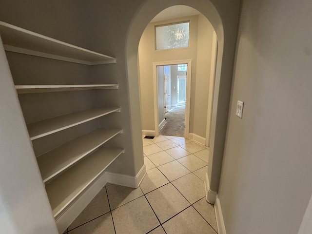 corridor featuring baseboards, arched walkways, and light tile patterned flooring