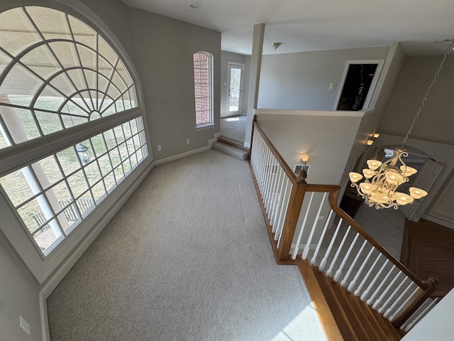 corridor with baseboards, carpet floors, an inviting chandelier, and an upstairs landing