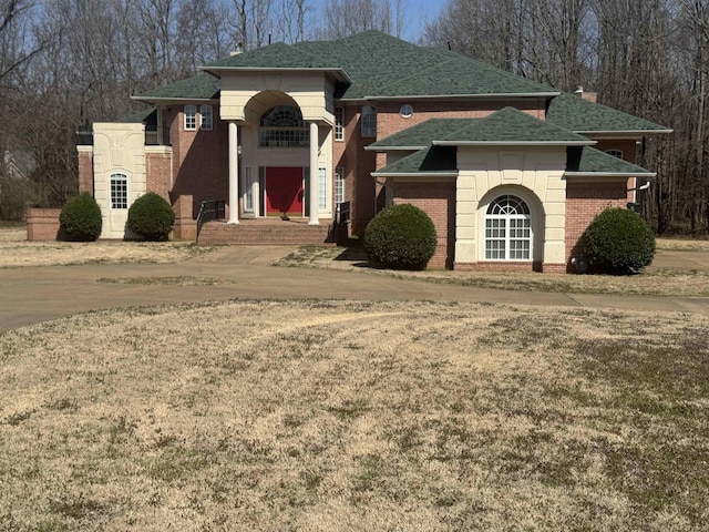 view of front of property featuring brick siding, roof with shingles, and a chimney