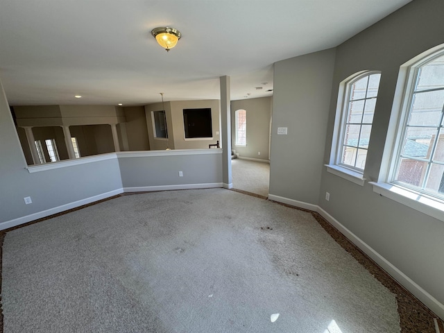 unfurnished living room with plenty of natural light, carpet flooring, and baseboards