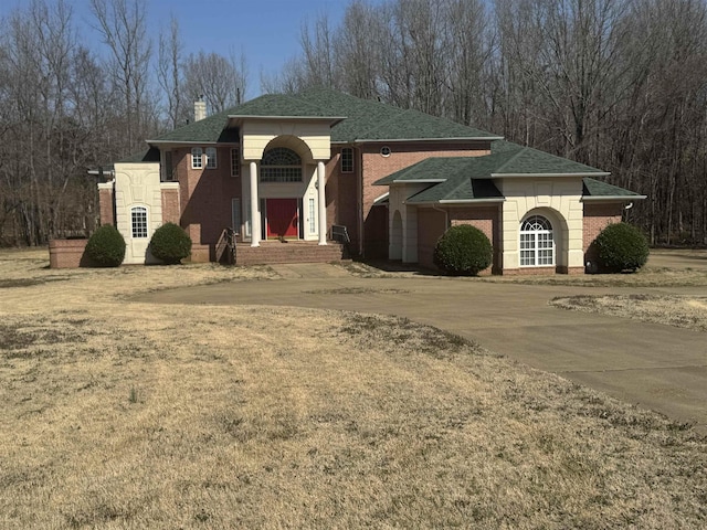 view of front of home featuring a shingled roof, concrete driveway, brick siding, and a chimney